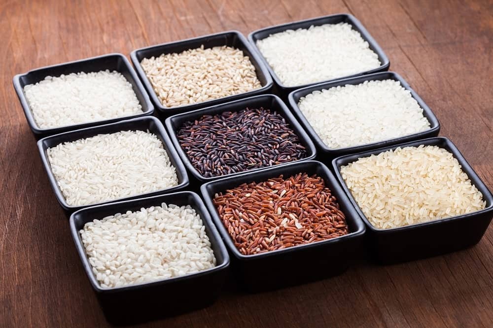 Various types of rice in black square bowls in the wooden table.