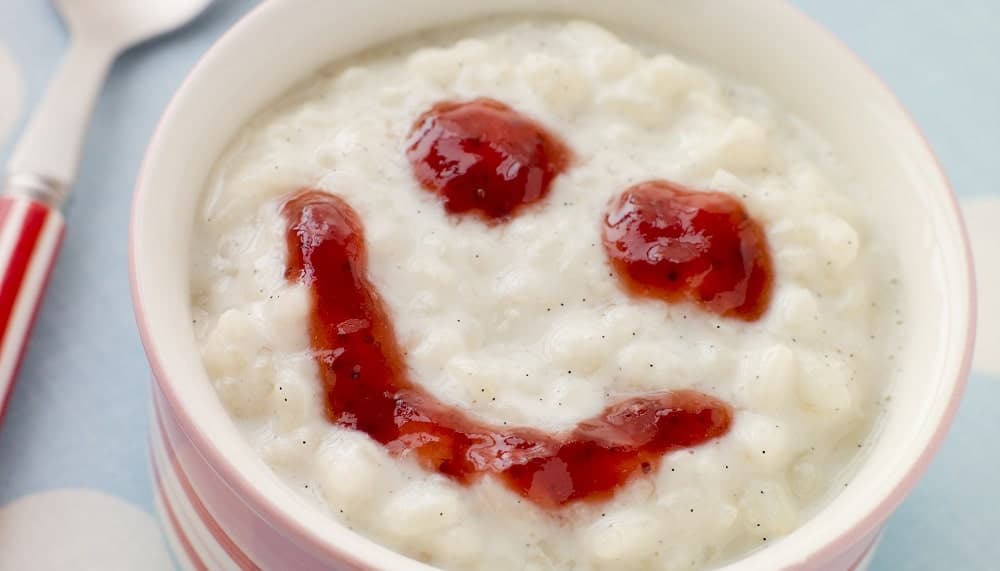 Bowl of creamed rice topped with Strawberry Jam smiley face.