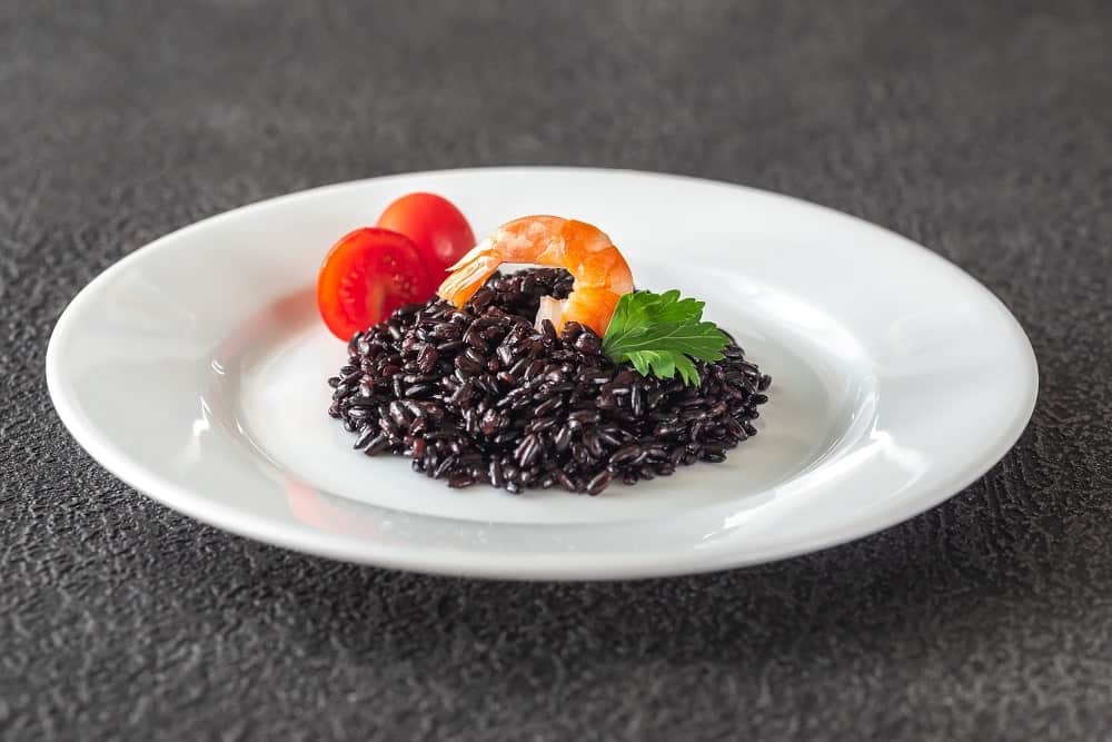 A plating of Black Rice, tomato and shrimp in a white plate.