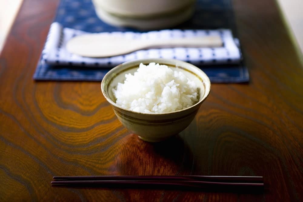 This is a small bowl of steamed white rice on a wooden table.