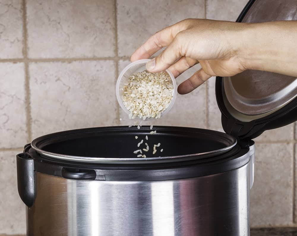 Grain of rice being put in an open rice cooker.